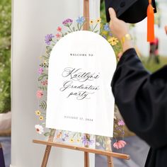 a person in a graduation cap and gown is placing a sign on a easel