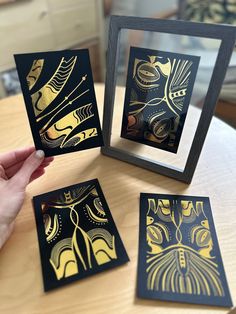 a person holding up four cards with gold foil designs on them in front of a mirror