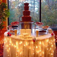 a table topped with lots of desserts next to a window filled with trees and lights