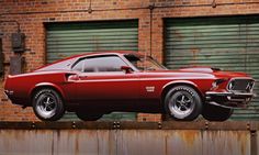 a red muscle car is parked on top of a rusted metal structure in front of a brick building