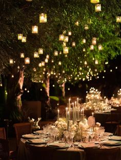 an outdoor dinner table with candles and flowers in the center, surrounded by greenery