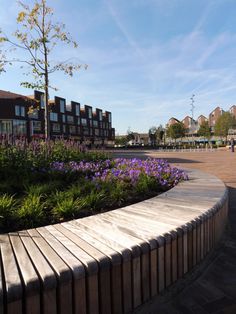 a wooden bench sitting in the middle of a flower garden next to a building with lots of windows