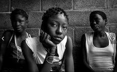 three women sitting next to each other in front of a brick wall with their hands on their chins