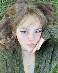 a woman laying in the grass with her hand on her head and looking at the camera