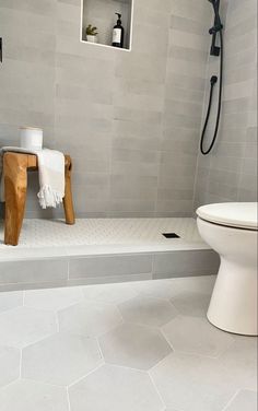 a white toilet sitting next to a wooden stool in a bathroom under a shower head