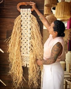 a woman holding up a piece of art made out of straw and other things that are hanging on the wall