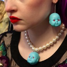 a woman with purple hair wearing blue and white beads, red lipstick and an earring