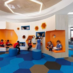 children are sitting and reading in the play area at an indoor learning center with hexagonal walls