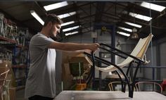 a man is working on a chair in a shop with other chairs and tables behind him