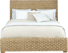 the bed is made up with white linens and wicker headboard, along with several pillows