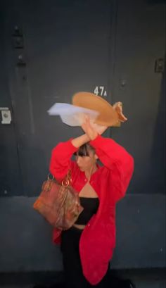 a woman in a red jacket and black pants holding a hot dog over her head