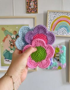 a hand is holding some crocheted flowers in front of pictures on the wall