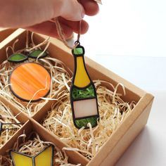 a hand is holding a stained glass bottle ornament in a box with straw