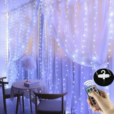 a person holding a remote control in front of a curtain with lights on it and a table