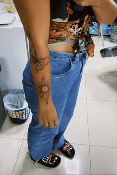 a person with a sun tattoo on their arm and foot, standing in front of a white tiled floor