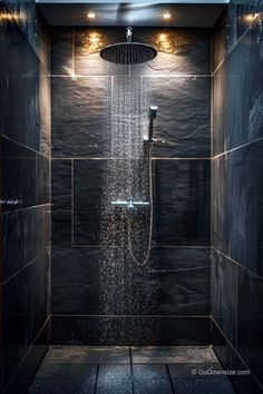 a shower head with rain coming from it in a black tiled bathroom, surrounded by wood flooring