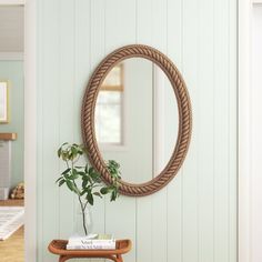 a round rope mirror hangs on the wall above a small table with a potted plant