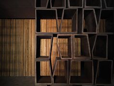 a bookshelf made out of wooden blocks and wood slats in front of a bamboo wall