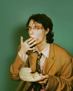 a man in a suit and tie eating cake with frosting on his face while holding a piece of cake