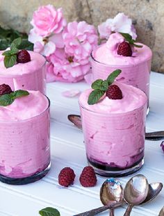 three desserts with raspberry frosting and fresh berries on the table next to pink flowers