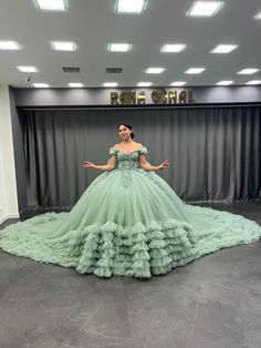 a woman in a green ball gown standing on a stage with her hands out to the side