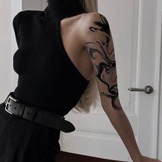 a woman with tattoos on her arm and shoulder standing in front of a white door