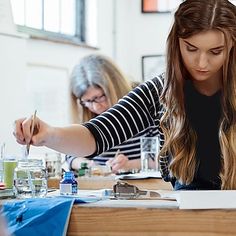 two women sitting at a table doing art work