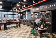 two men working on washing machines in a large laundry room with black and white checkered flooring