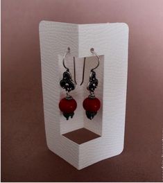 a pair of red and black earrings in a white display case on a brown background