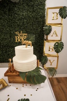 a white cake sitting on top of a wooden table next to a green leafy wall