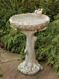 a birdbath sitting on top of a cement slab in front of some bushes