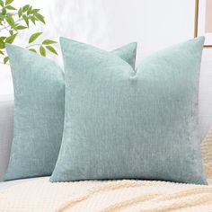 two light blue pillows sitting on top of a couch next to a potted plant