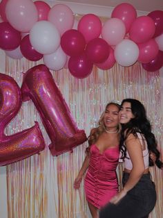 two women standing next to each other in front of balloons and streamers with the number twenty on it