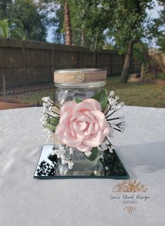 a pink flower in a jar sitting on top of a white table cloth covered table