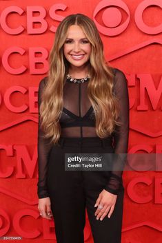 a woman in black outfit standing on red carpet with long hair and wearing high heels