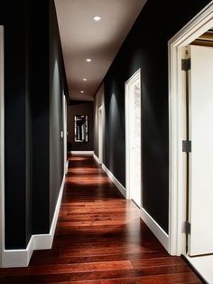 a long hallway with black walls and white trim on the wall, wood flooring