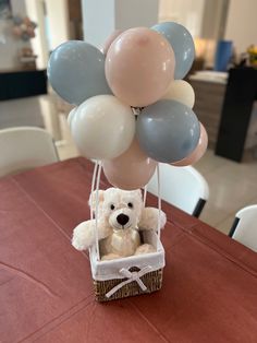 a teddy bear in a basket with balloons on the table at a party or celebration