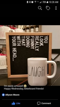 a white coffee mug sitting next to a black board with the words laugh on it