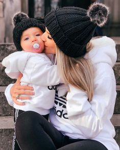 a woman holding a baby while wearing a hat and kissing her face on the cheek