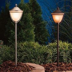 two lamps are sitting on the ground in front of some bushes