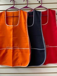 three aprons hanging from hooks on a wall, one in orange and the other in blue