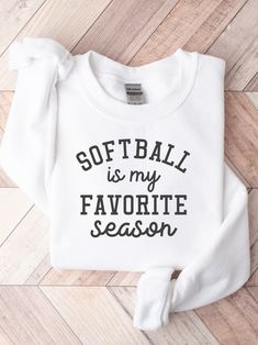 a white sweatshirt with the words softball is my favorite season on it, sitting on a wooden floor