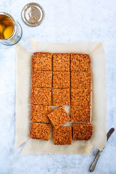 an image of granola bars cut into squares on parchment paper next to glasses and spoons