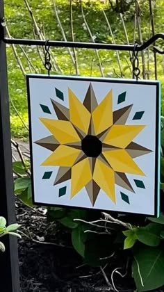 a yellow and brown sunflower is hanging from a black metal frame in front of some green plants