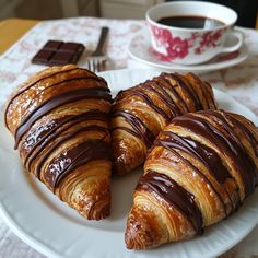 chocolate covered croissants on a white plate next to a cup of coffee