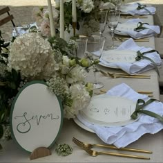 the table is set with white flowers and place settings