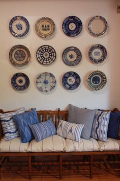 a couch with pillows and plates on the wall above it in front of a wooden bench