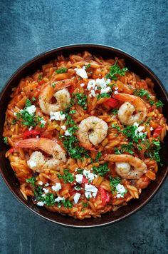 pasta with shrimp, tomatoes and feta cheese in a brown bowl on a blue surface