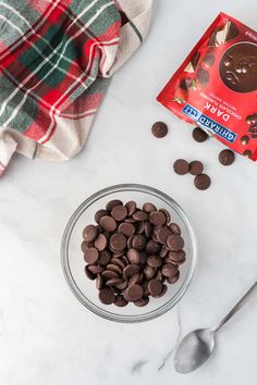 chocolate chips in a glass bowl next to a spoon and napkin on a marble surface