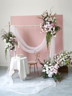 a table with flowers on it next to a pink wall and white draping